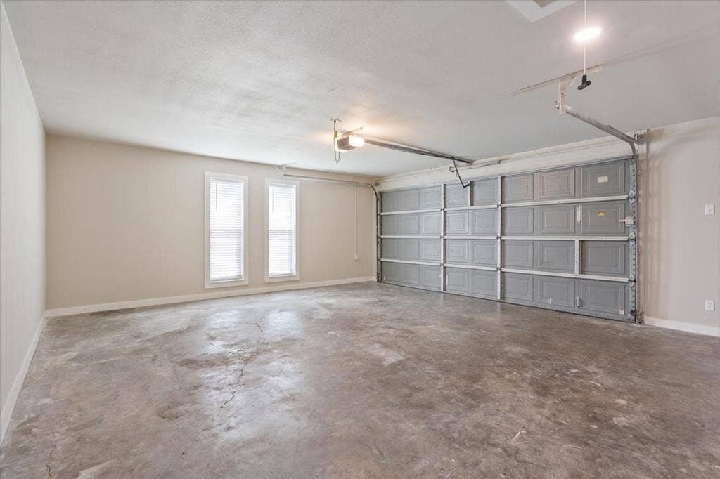 116 Boleman Drive, Hewitt, TX 76643 Spacious two-car garage featuring a gray sectional garage door, concrete flooring, storage closed, and two windows with blinds