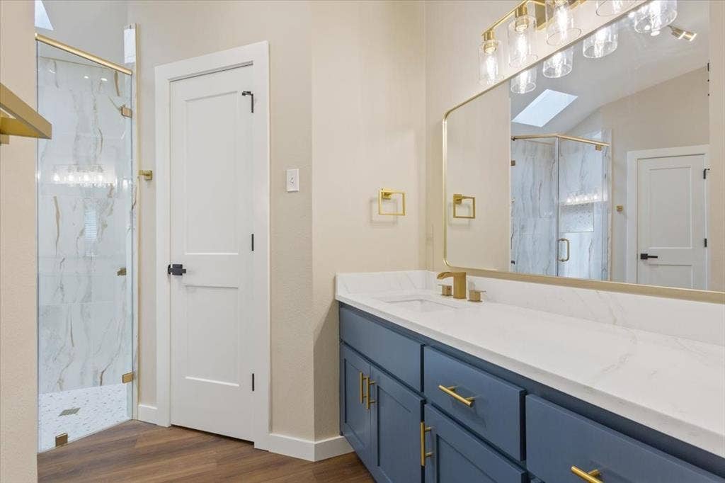 116 Boleman Drive, Hewitt, TX 76643 Primary ensuite bathroom featuring a large walk-in shower with custom glass, spacious vanity with blue cabinetry, gold-tone hardware, and a white quartz countertop