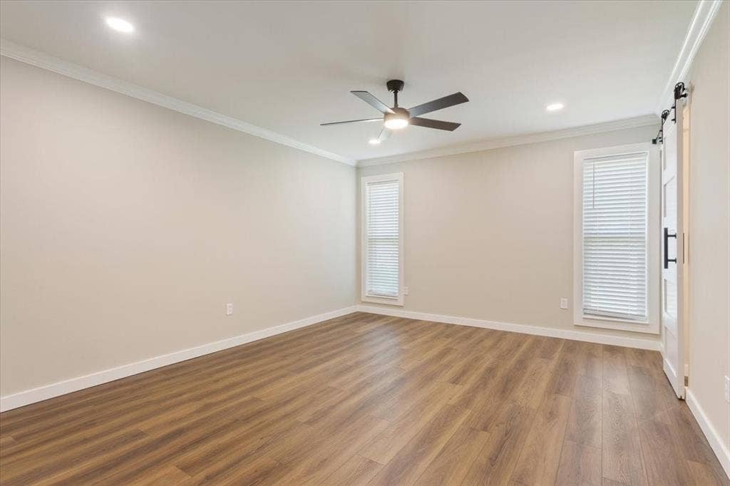116 Boleman Drive, Hewitt, TX 76643 Spacious primary bedroom featuring LVP wood-finish flooring, barn-door access to the ensuite bathroom,two large windows with blinds, a ceiling fan with integrated lighting, and recessed ceiling lights