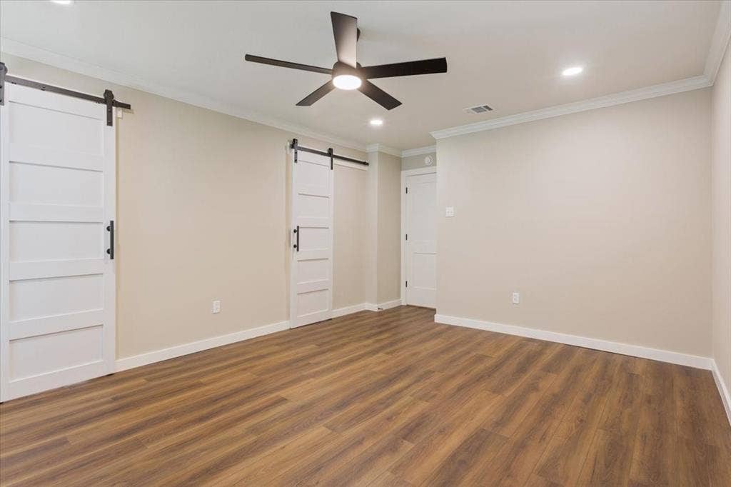 116 Boleman Drive, Hewitt, TX 76643 Spacious primary bedroom featuring LVP wood-finish flooring, barn-door access to the ensuite bathroom, a ceiling fan with integrated lighting, and recessed ceiling lights