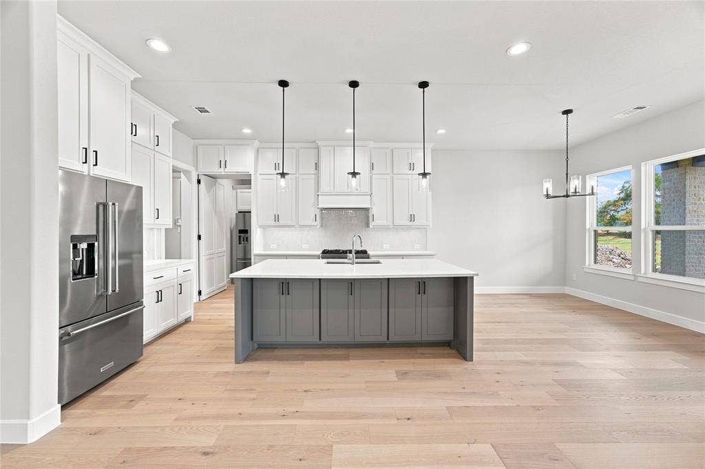 3820 Jacks Loop, Midlothian, TX 76065 Kitchen featuring a large island with gray cabinetry, stainless steel appliances, white perimeter cabinetry, light wood-finish flooring, and recessed lighting. Butler pantry open.