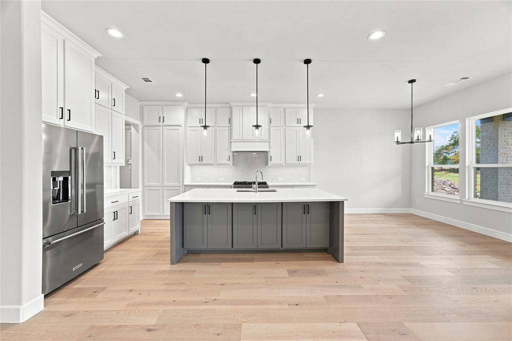 3820 Jacks Loop, Midlothian, TX 76065 Contemporary kitchen with stainless steel appliances, light wood-finish flooring, and a gray island with a light countertop. Butler pantry door closed.