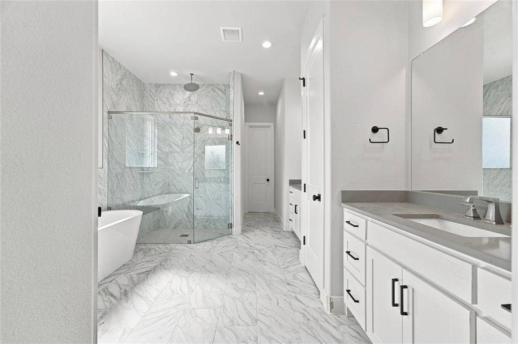 3820 Jacks Loop, Midlothian, TX 76065 Freestanding soaking tub, frameless glass shower enclosure, dual vanity with undermount sinks, stone countertops, and marble-look tile flooring