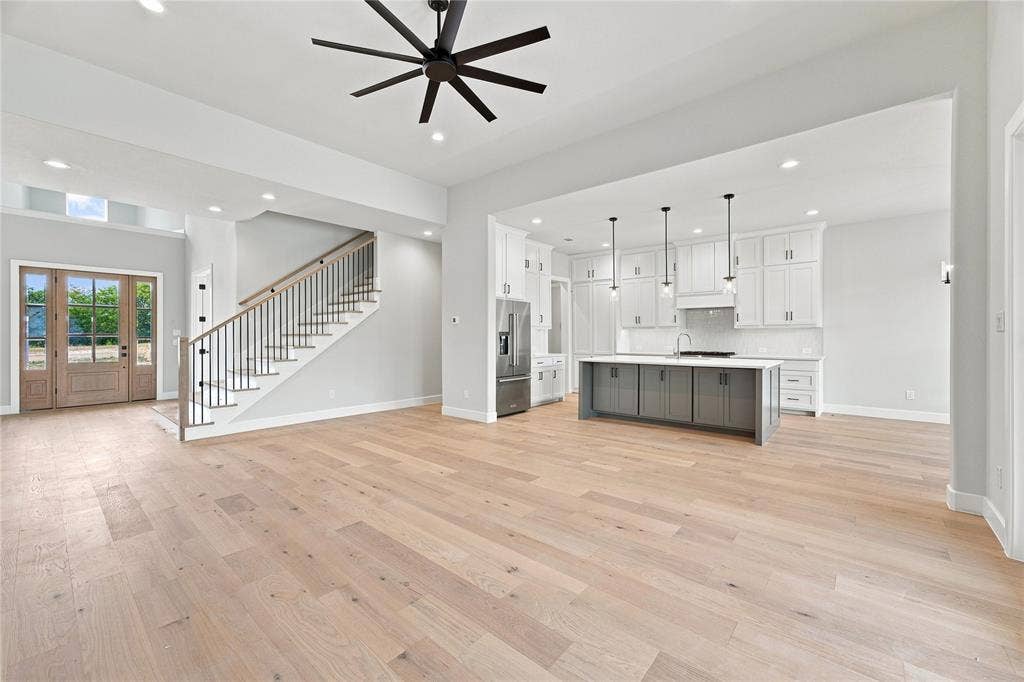 3820 Jacks Loop, Midlothian, TX 76065 Open-concept living area featuring wood-finish flooring, a modern kitchen island with pendant lighting, white cabinetry, a stainless steel refrigerator, and a staircase with metal balusters