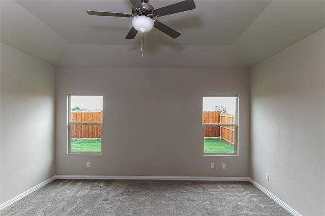 448 Ella Lane, Fate, TX 75087 Spacious room featuring a tray ceiling with a ceiling fan and light fixture, two windows, gray carpeting, and white baseboards
