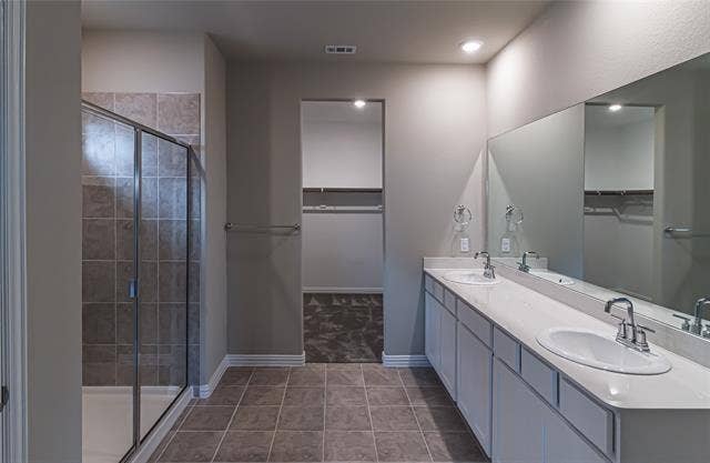 448 Ella Lane, Fate, TX 75087 Bathroom featuring a dual vanity with white cabinetry and integrated sinks, a large wall-mounted mirror, recessed lighting, and a walk-in shower with tile surround and glass enclosure
