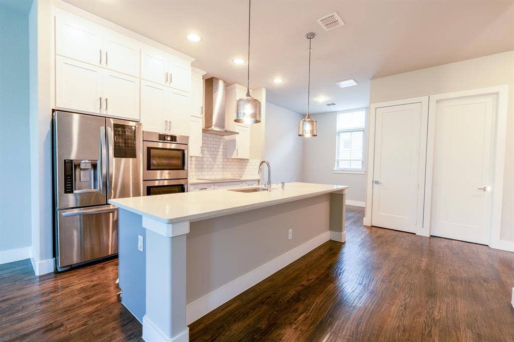 2514 Vintage Street, Farmers Branch, TX 75234 Modern kitchen featuring stainless steel appliances, white cabinetry, a large center island with a built-in sink, pendant lighting, and wood-finish flooring