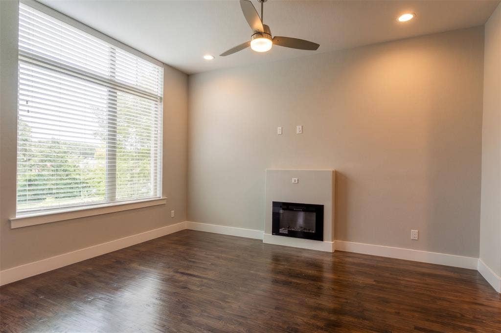 2514 Vintage Street, Farmers Branch, TX 75234 Spacious living room featuring wood-finish flooring, a contemporary built-in electric fireplace, and expansive windows fitted with blinds