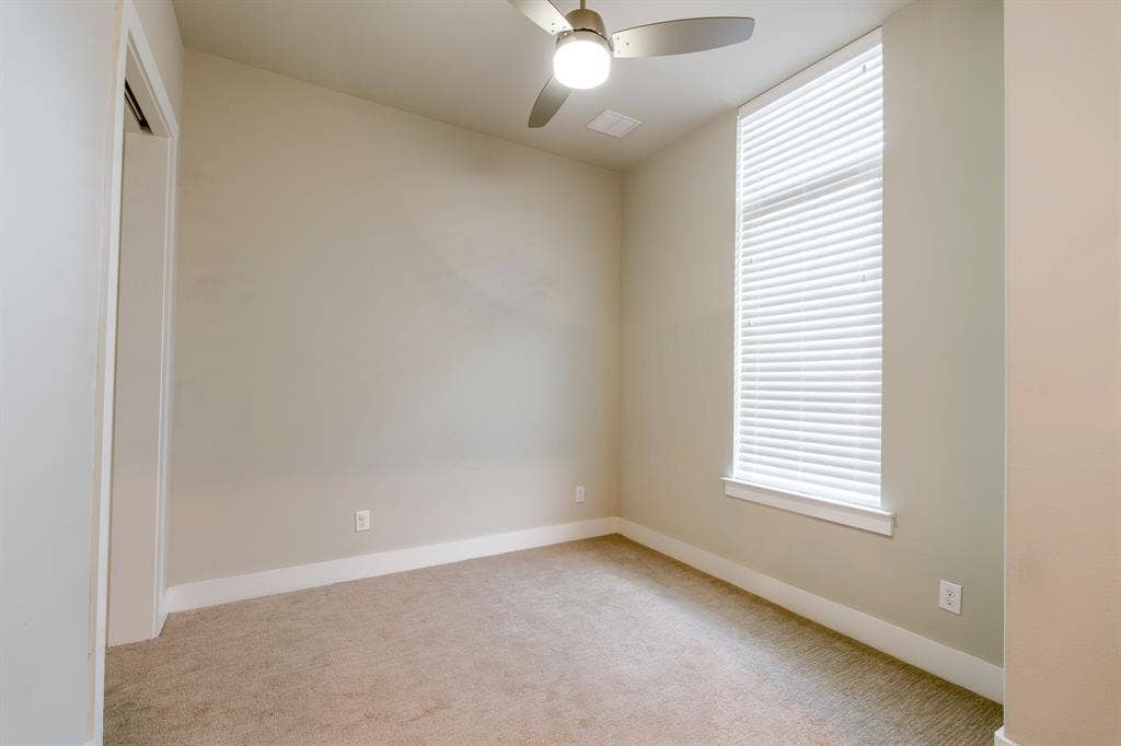 2514 Vintage Street, Farmers Branch, TX 75234 Third floor bedroom: Neutral-toned room featuring a tall window with white blinds, carpet flooring, a ceiling fan with integrated lighting, and white baseboards