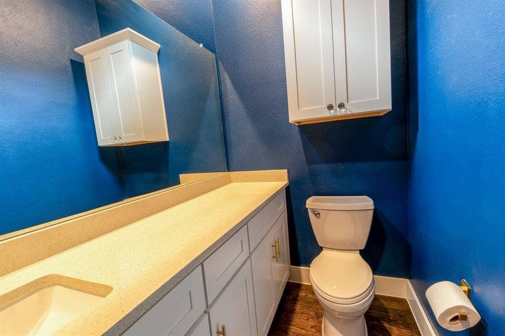 2514 Vintage Street, Farmers Branch, TX 75234 2nd Floor half-bathroom featuring a vanity with an integrated sink, quartz countertop, a full-width mirror, white cabinetry, a wall-mounted storage cabinet, and wood-finish flooring