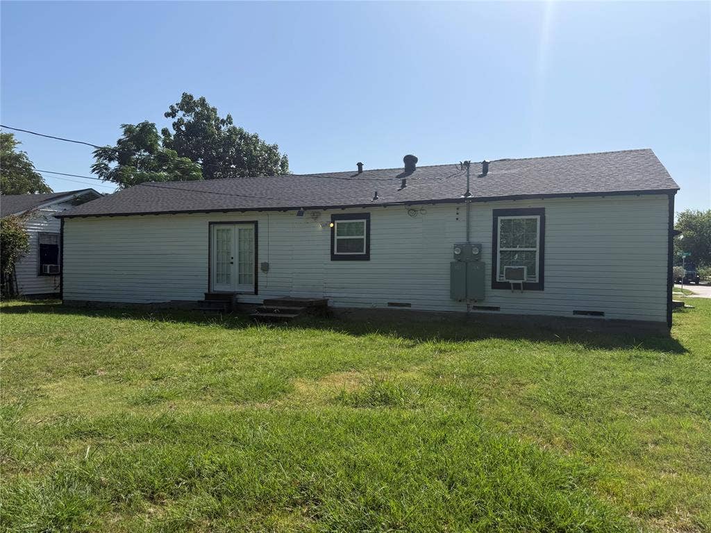 205 22nd Street, Grand Prairie, TX 75050 Rear exterior featuring light-colored siding, a dark asphalt shingle roof, and a grassy yard