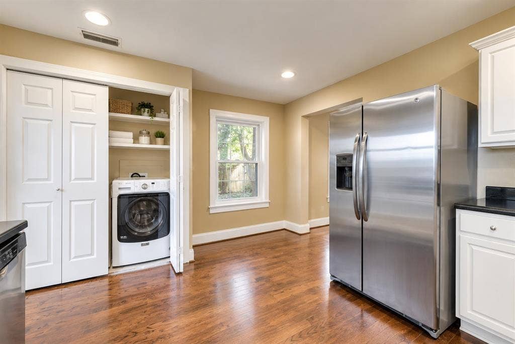 Built-in laundry closet with shelving, stainless steel side-by-side refrigerator, wood-finish flooring, recessed lighting, and white cabinetry with a dark countertop