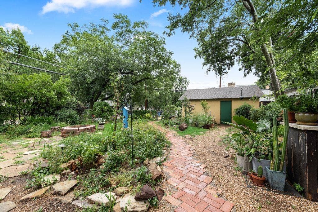 Expansive backyard featuring a stone patio, brick fire pit, and mature trees providing natural shade