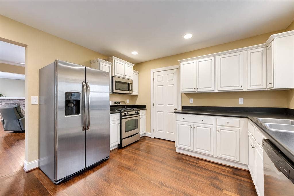 Kitchen featuring wood-finish flooring, white cabinetry, dark countertops, and stainless steel appliances