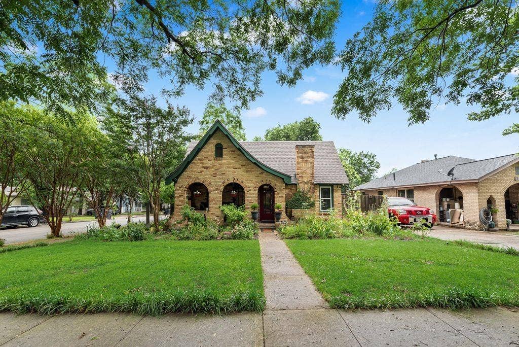 Stone facade residence featuring a front gabled roof, arched front porch openings, prominent brick chimney, and a pedestrian walkway leading to the entrance