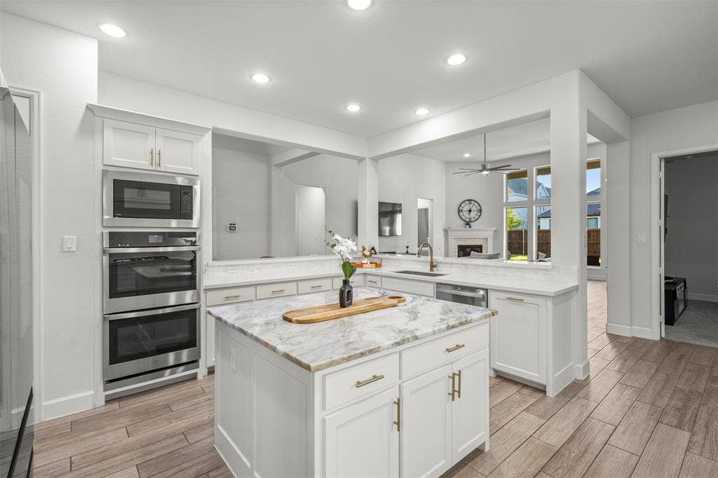 2837 Midlake Drive, Midlothian, TX 76065 Kitchen featuring an eat-at island with a stone countertop, stainless steel appliances including a built-in microwave and double ovens, white cabinetry, and wood-finish flooring