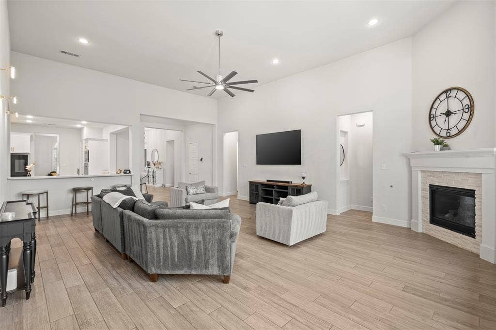 2837 Midlake Drive, Midlothian, TX 76065 Spacious living area featuring high vaulted ceilings, wood-finish flooring, a contemporary ceiling fan, recessed lighting, and a fireplace with a stone surround and white mantel