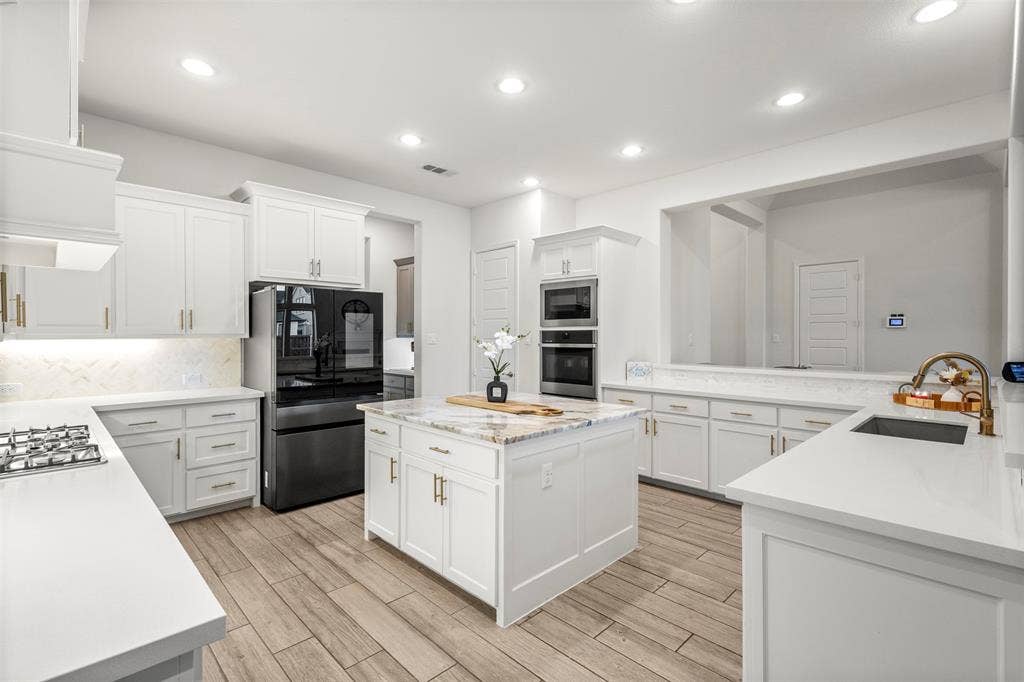 2837 Midlake Drive, Midlothian, TX 76065 Gourmet kitchen featuring a central island with a granite countertop, white cabinetry with brass hardware, wood-finish flooring, built-in double ovens, and a gas cooktop