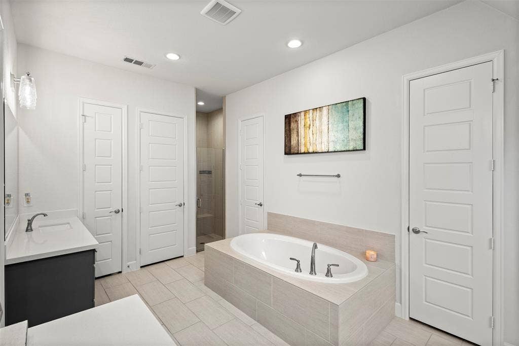 2837 Midlake Drive, Midlothian, TX 76065 Soaking tub featuring a tiled surround, dual-sink vanity with quartz countertop, walk-in shower with glass enclosure, recessed lighting, and large format tile flooring