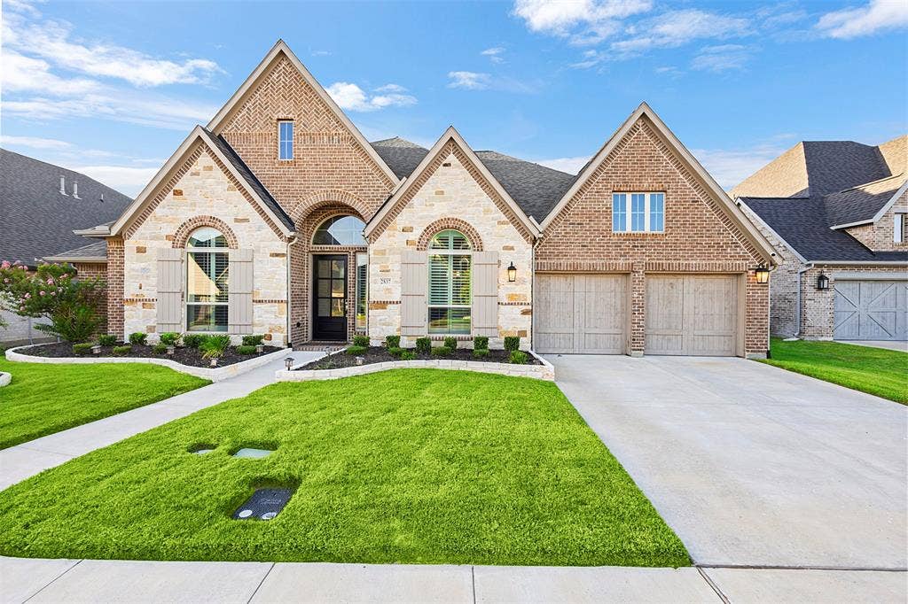 2837 Midlake Drive, Midlothian, TX 76065 Brick and stone facade featuring arched entryways, a two-car garage with wood-finish doors, prominent gables, and a manicured lawn with a concrete walkway