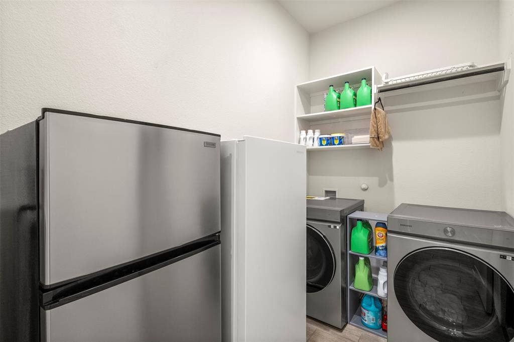 2837 Midlake Drive, Midlothian, TX 76065 Dedicated utility space featuring a stainless steel refrigerator, washer and dryer appliances, white wall shelving, and an integrated hanging rod
