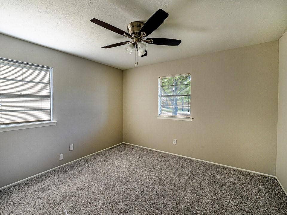 1205 Northridge Drive, Plano, TX 75075 Spacious bedroom showcasing neutral wall finishes, plush carpeting, ceiling fan with integrated lighting, and dual windows providing natural light