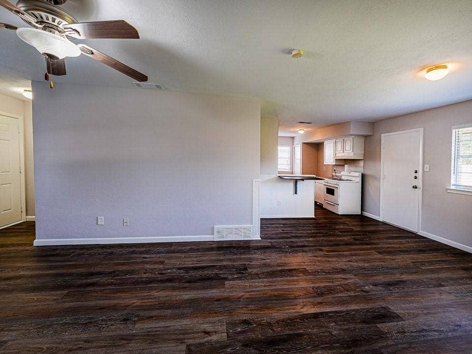 1205 Northridge Drive, Plano, TX 75075 Open living area featuring dark wood-finish flooring, ceiling fan with integrated lighting, and seamless access to a kitchen with white cabinetry and stainless steel appliances