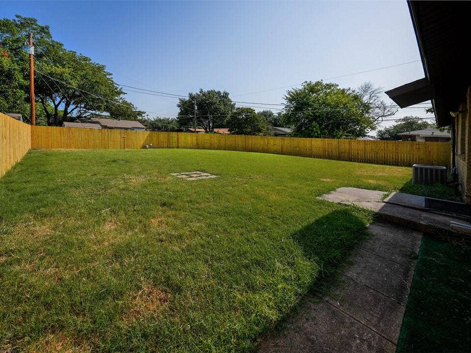 1205 Northridge Drive, Plano, TX 75075 Expansive backyard featuring a manicured lawn enclosed by wood-finish fencing, mature shade trees, concrete patio area, and direct access from the home's rear exit