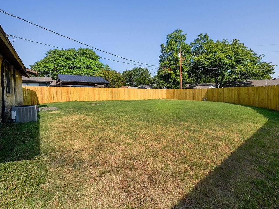 1205 Northridge Drive, Plano, TX 75075 Expansive backyard featuring a level lawn bordered by wood privacy fencing, mature shade trees, and clear sightlines across the grounds