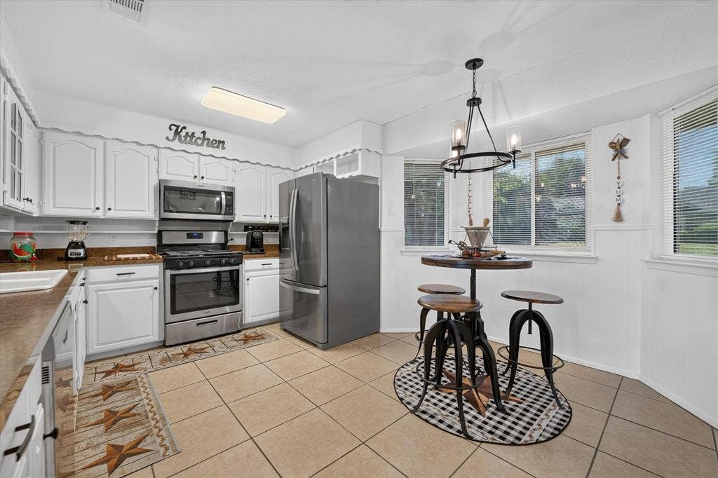 629 Newton Drive, Burleson, TX 76028 Bright and spacious kitchen featuring stainless steel appliances, white cabinetry with hardware accents, wood-finish countertops, and tile flooring