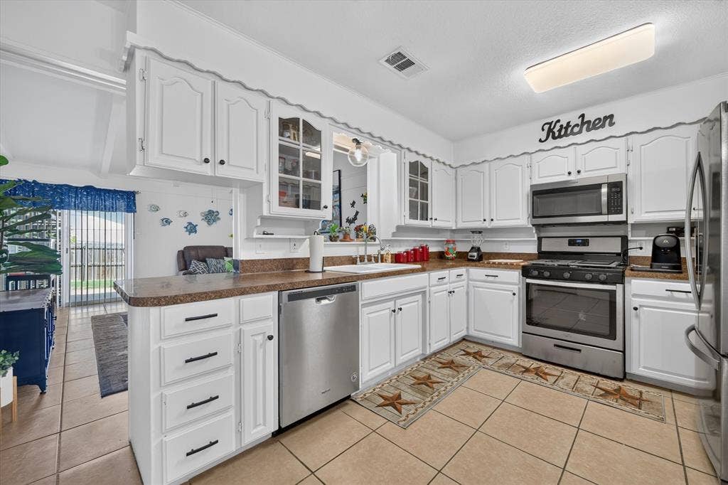 629 Newton Drive, Burleson, TX 76028 Kitchen featuring white cabinetry with dark hardware, stainless steel appliances, and a tile floor