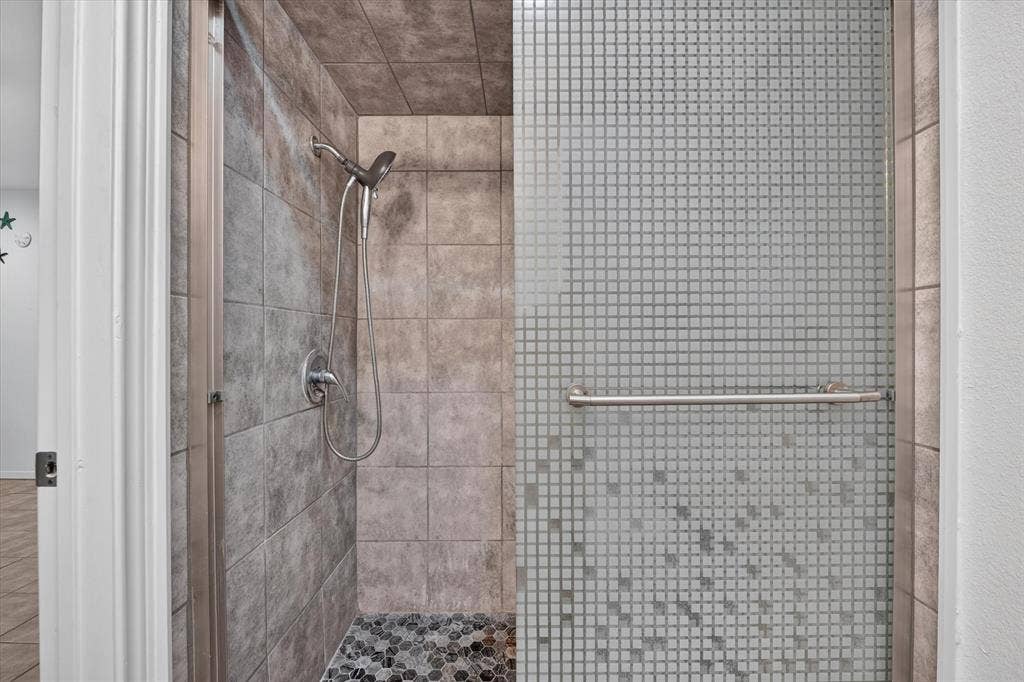 629 Newton Drive, Burleson, TX 76028 Spa-inspired shower enclosure featuring large-format tile walls, small-scale mosaic tile accents, and a rainfall showerhead with handheld spray fixture