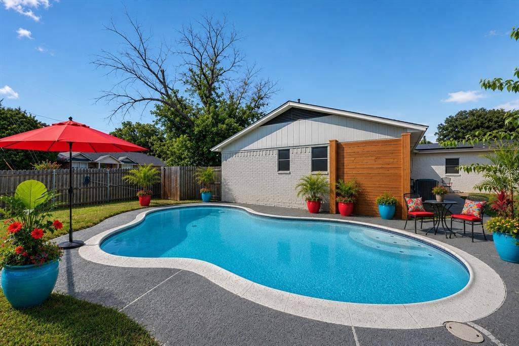 629 Newton Drive, Burleson, TX 76028 Virtually staged Stunning resort-style backyard oasis featuring a freeform saltwater pool with curved concrete decking, surrounded by mature landscaping and vibrant planters