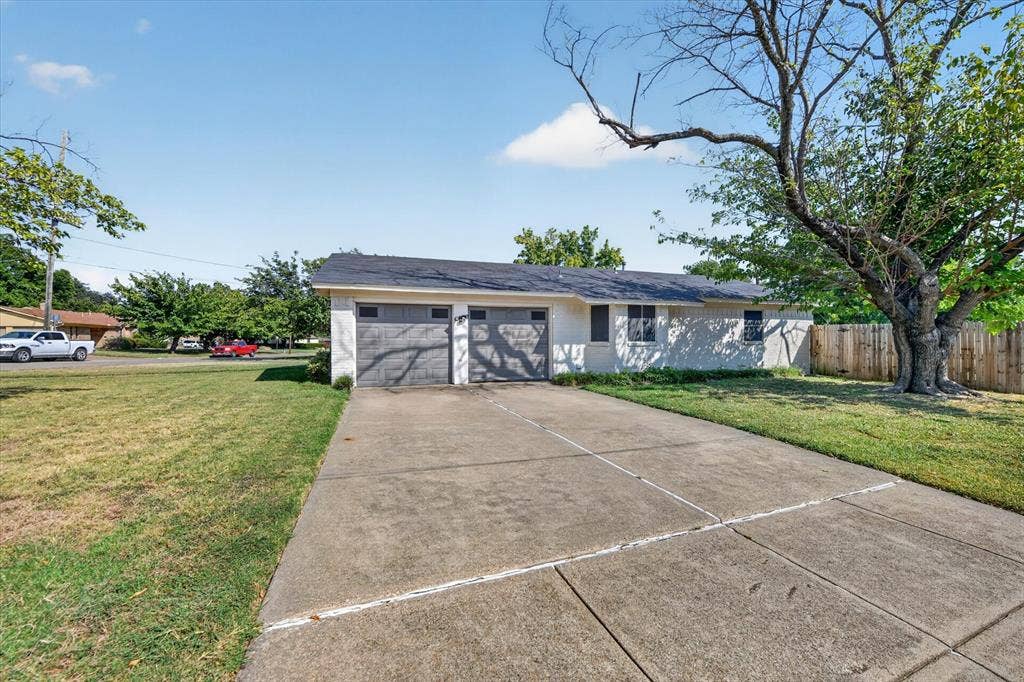 629 Newton Drive, Burleson, TX 76028 Single-story residence featuring a concrete driveway, attached two-car garage with panel doors, and a wood privacy fence