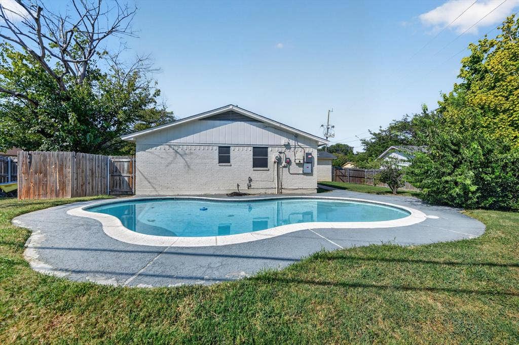 629 Newton Drive, Burleson, TX 76028 Backyard oasis featuring a curved in-ground swimming pool with concrete decking, surrounded by mature landscaping and lush lawn