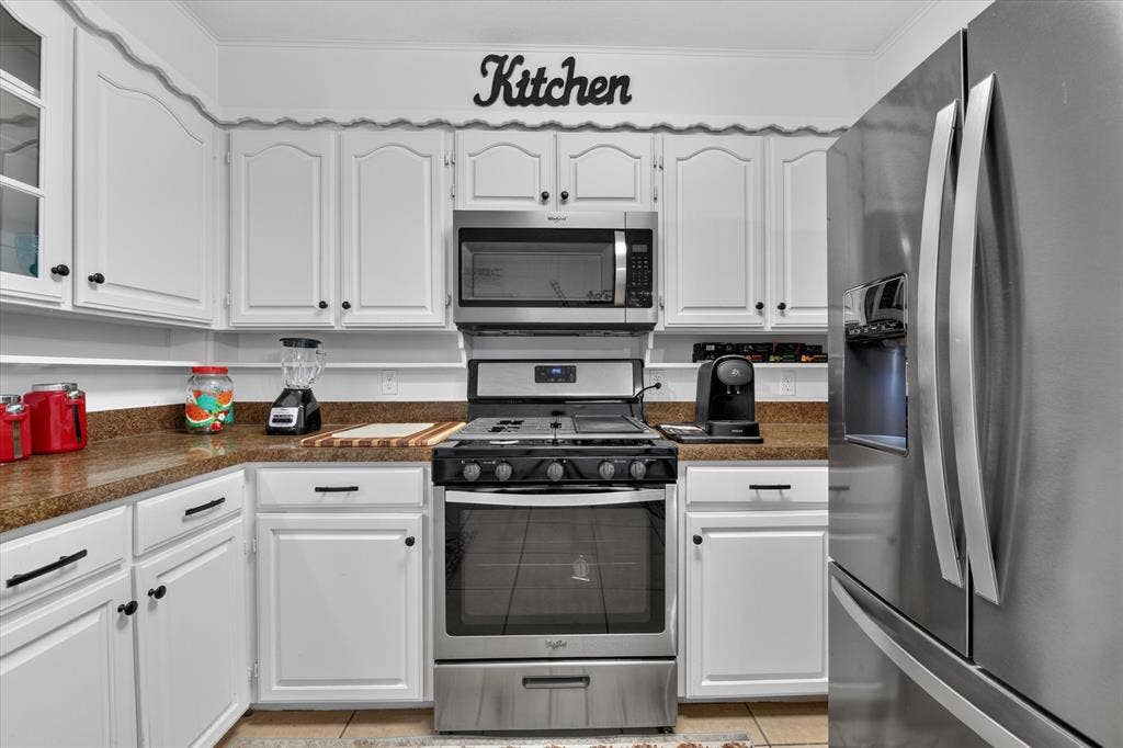 629 Newton Drive, Burleson, TX 76028 Bright, updated kitchen featuring white cabinetry with hardware accents, stainless steel appliances including a gas range with convection oven and over-the-range microwave, and granite countertops