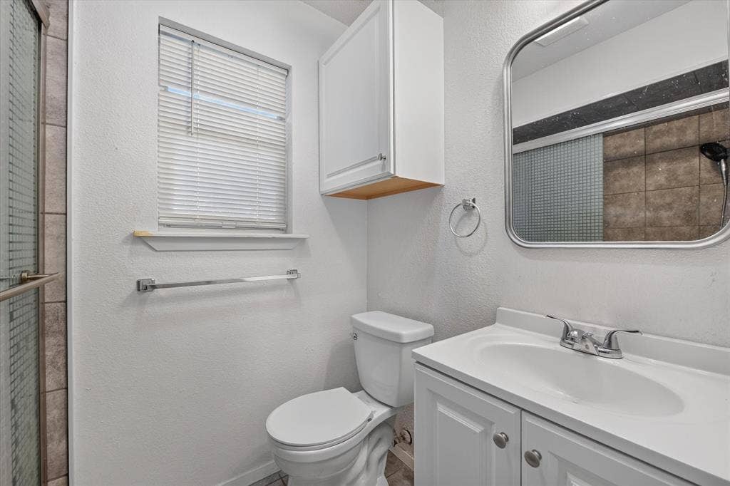 629 Newton Drive, Burleson, TX 76028 Bathroom featuring a white vanity with integrated sink, chrome fixtures, framed mirror, and an overhead storage cabinet