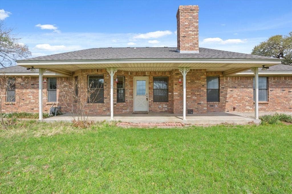 146 Indian Paint Brush Road, Eddy, TX 76524 Rear exterior featuring a covered patio, brick facade, a prominent brick chimney, and a dark shingle roof