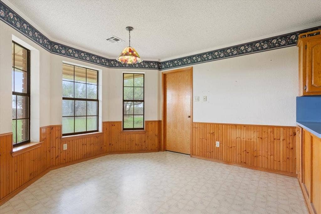 146 Indian Paint Brush Road, Eddy, TX 76524 Dining space featuring three large windows, wood-finish wainscoting, and patterned vinyl flooring