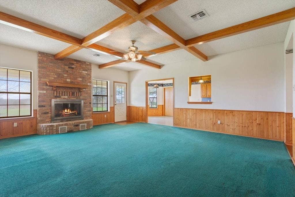 146 Indian Paint Brush Road, Eddy, TX 76524 Spacious living area featuring a brick-surround fireplace with a wood mantel, exposed wood ceiling beams, and wood paneling along the lower walls