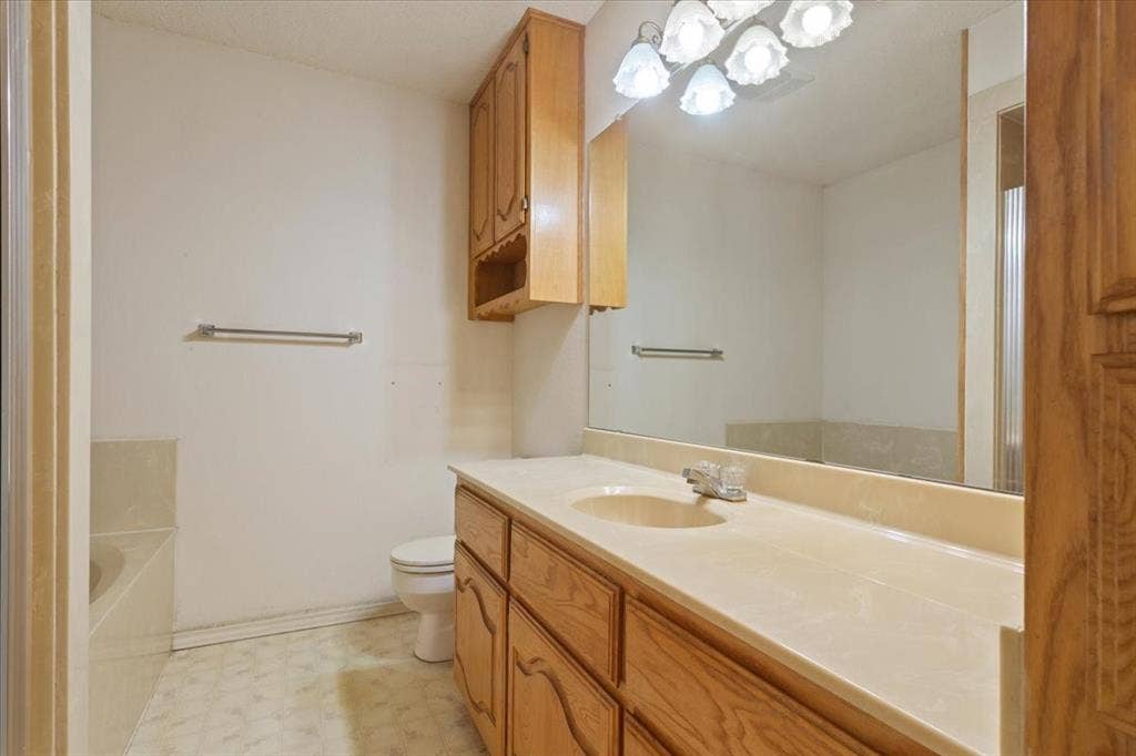 146 Indian Paint Brush Road, Eddy, TX 76524 Bathroom featuring a light-toned vanity with wood-finish cabinetry, an integrated sink, a large wall-mounted mirror, and a built-in tub