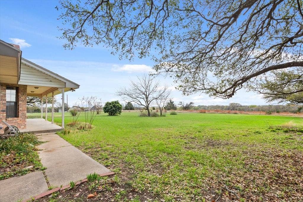 146 Indian Paint Brush Road, Eddy, TX 76524 Expansive green lawn with mature trees, a covered porch, and a concrete pathway