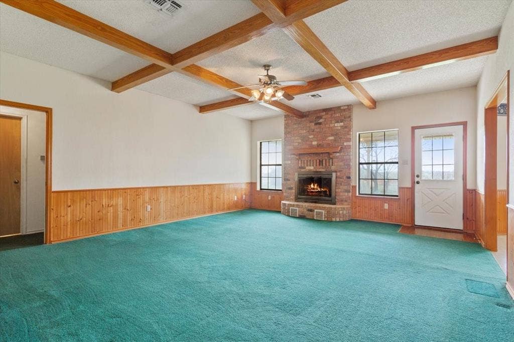 146 Indian Paint Brush Road, Eddy, TX 76524 Spacious living area featuring a brick fireplace, exposed wood ceiling beams, wood paneling, and multiple windows