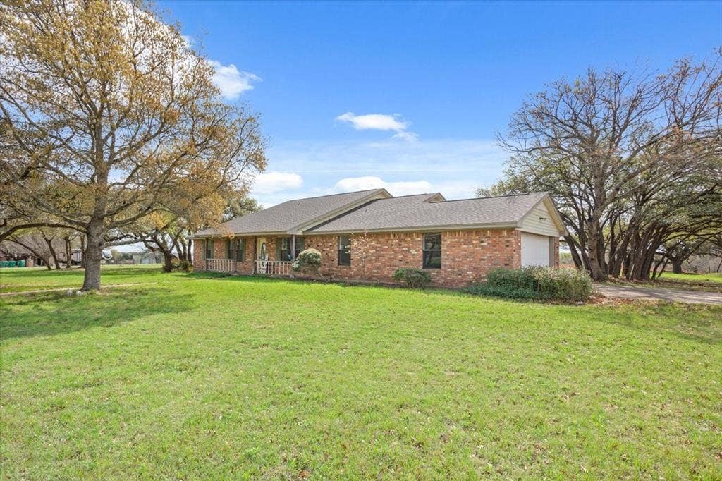 146 Indian Paint Brush Road, Eddy, TX 76524 Brick ranch-style residence featuring a covered front porch with white columns, a large attached garage, and a dark shingle roof