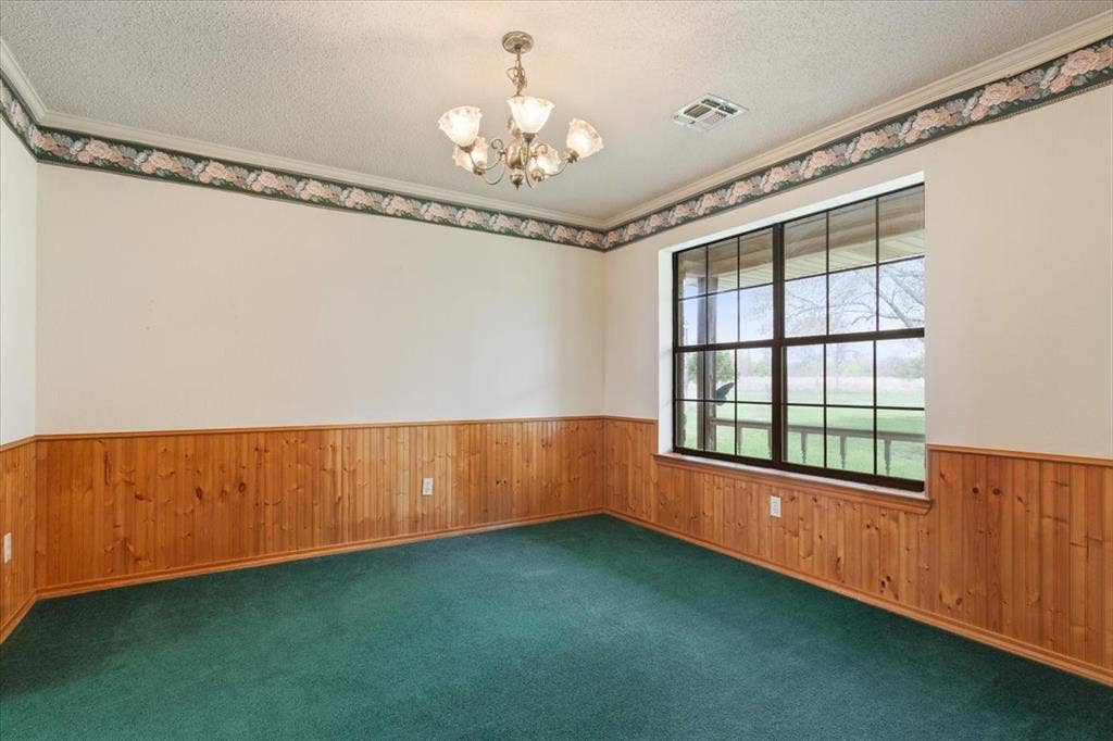 146 Indian Paint Brush Road, Eddy, TX 76524 Spacious room featuring wood paneling, a large multi-pane window, green carpeting, a decorative ceiling border, and a chandelier