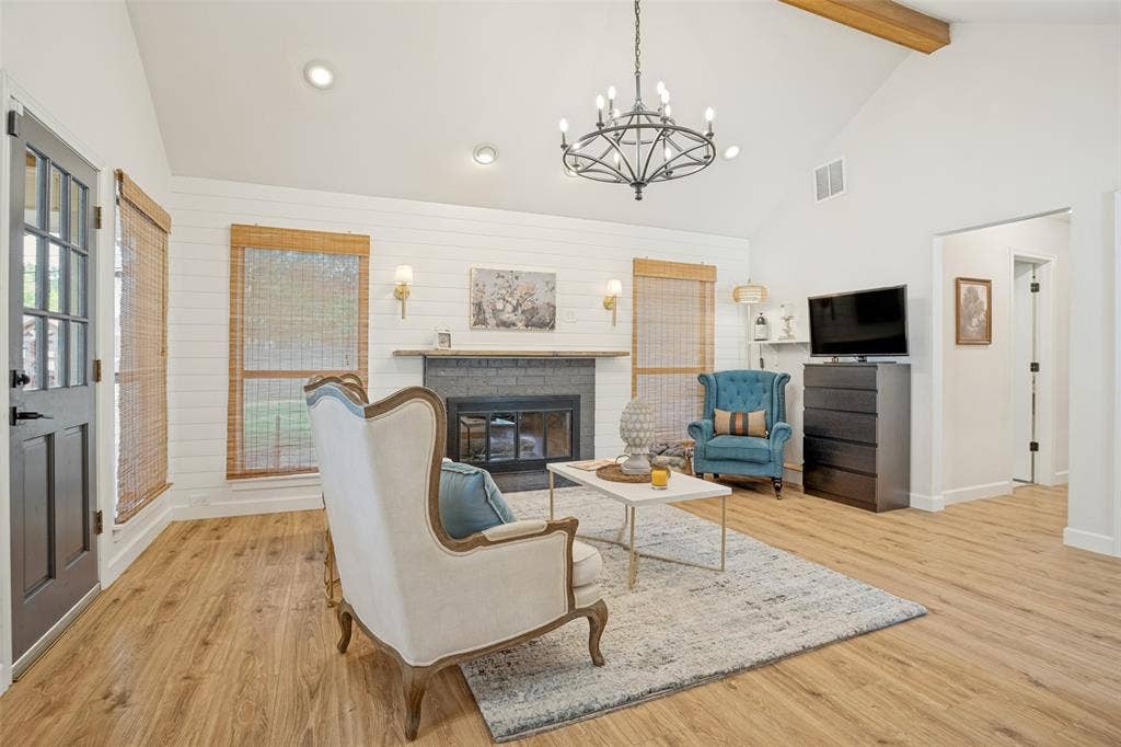 8201 Christie Drive, Frisco, TX 75033 Vaulted ceiling with an exposed wood beam, wood-finish flooring, white shiplap accent wall, fireplace with stone surround, and a dark-paneled door with glass inserts