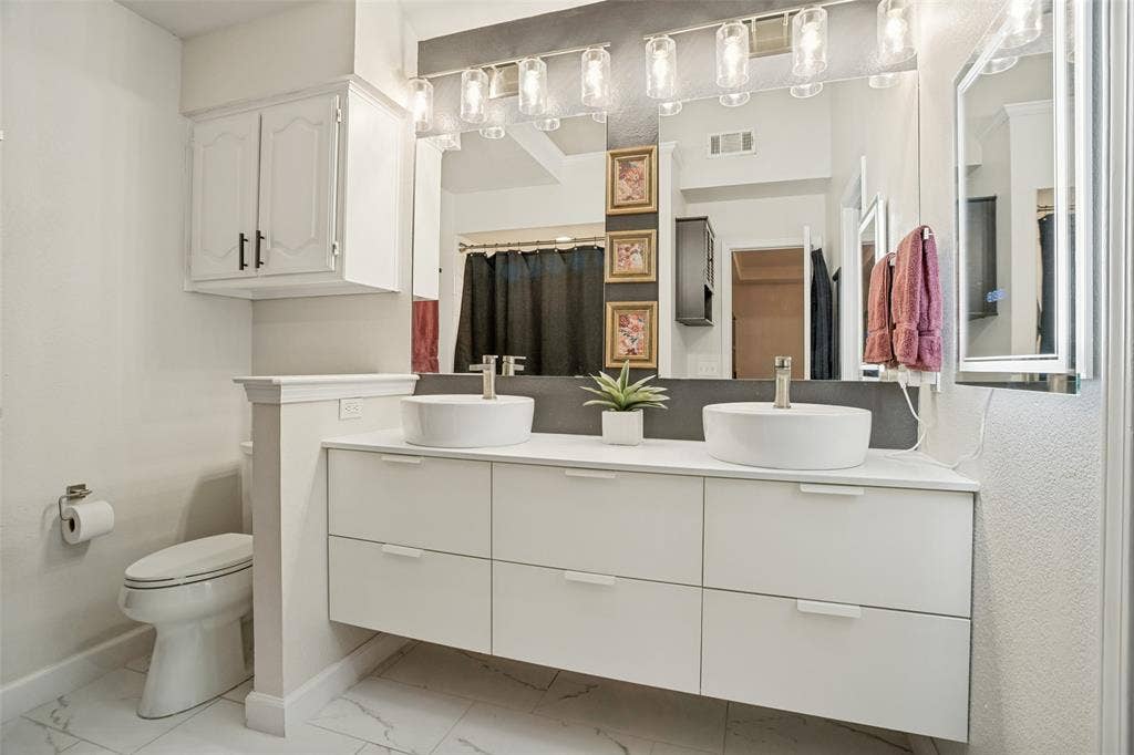 8201 Christie Drive, Frisco, TX 75033 Double vanity with white vessel sinks, a wall-mounted light fixture, and a large mirror