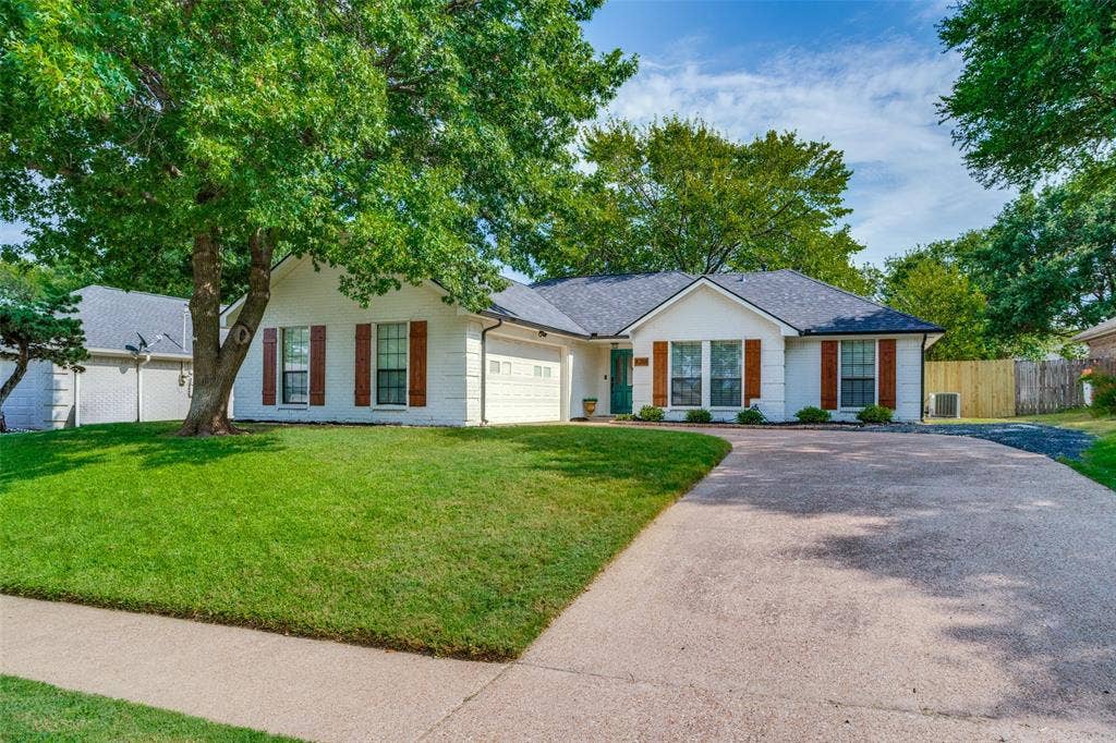 8201 Christie Drive, Frisco, TX 75033 White exterior featuring a dark asphalt shingle roof, brown decorative shutters, a light-colored concrete driveway, and a manicured lawn