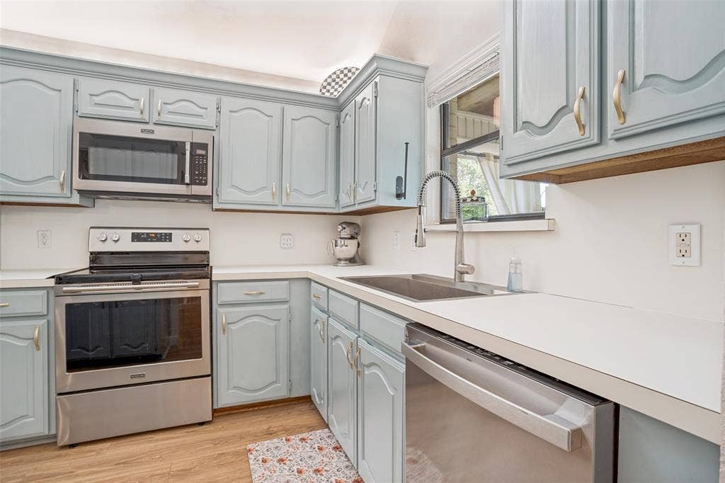 8201 Christie Drive, Frisco, TX 75033 Updated kitchen featuring light blue cabinetry with arched door details, stainless steel appliances including a slide-in range and dishwasher, undermount sink with gooseneck faucet, quartz countertops, wood-finish flooring, and ample storage with open shelving above the counter