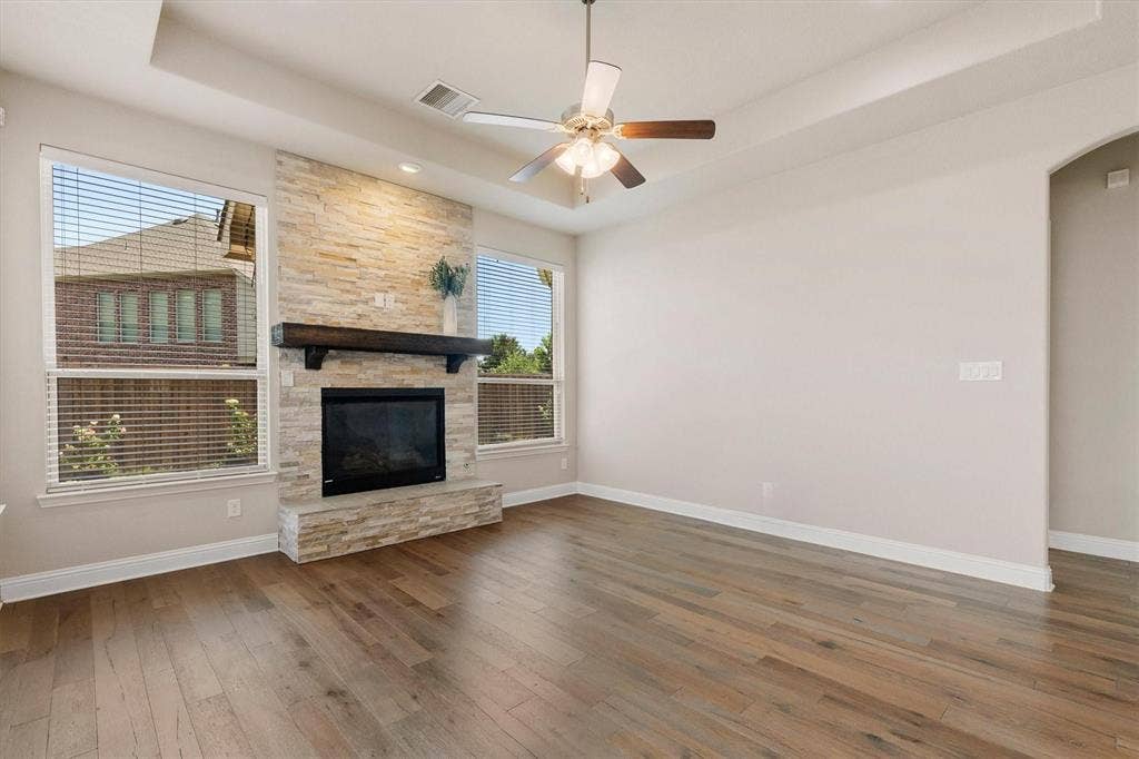4109 Rainey Street, McKinney, TX 75070 Stone-clad fireplace with a dark wood-finish mantel, wood-finish flooring, and a ceiling fan